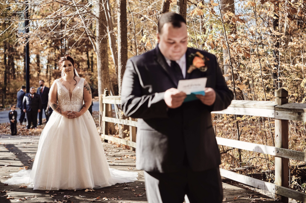 A bride looks on at her groom before he turns around to look at her for the first time on their wedding day. The groom reads some beautiful, touching words from his bride right before he turns around. At Flat Rock Community Center in Flat Rock, Michigan. Image taken by Erika Black Photography